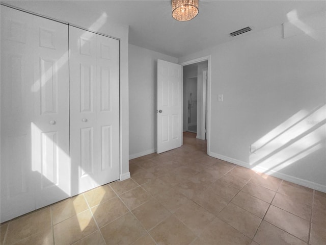 unfurnished bedroom with light tile patterned floors, a notable chandelier, and a closet