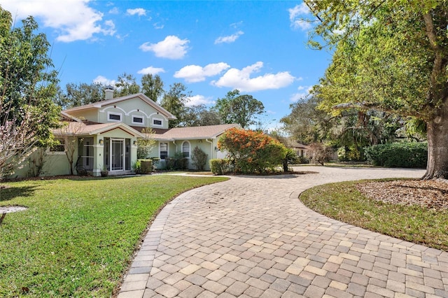 view of front of property featuring curved driveway, a chimney, and a front lawn