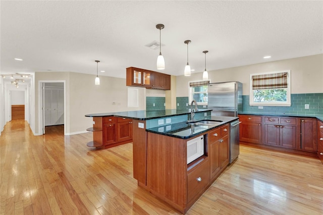 kitchen with dark stone counters, stainless steel appliances, a center island with sink, and decorative light fixtures