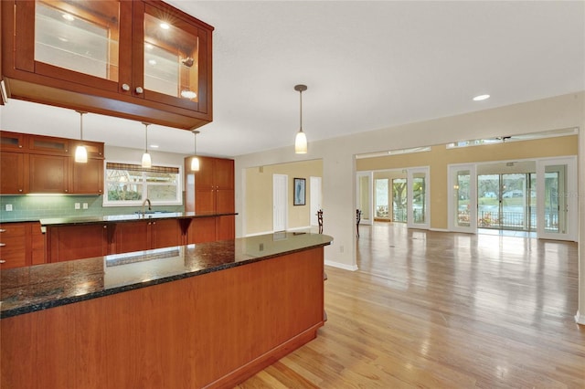 kitchen featuring hanging light fixtures, a healthy amount of sunlight, glass insert cabinets, and decorative backsplash