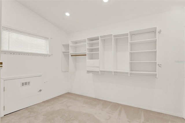 walk in closet with visible vents, vaulted ceiling, and light colored carpet