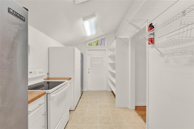 kitchen with light tile patterned floors, white range with electric stovetop, lofted ceiling, freestanding refrigerator, and white cabinetry