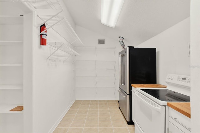 kitchen with light tile patterned floors, white range with electric stovetop, visible vents, a textured ceiling, and white cabinetry