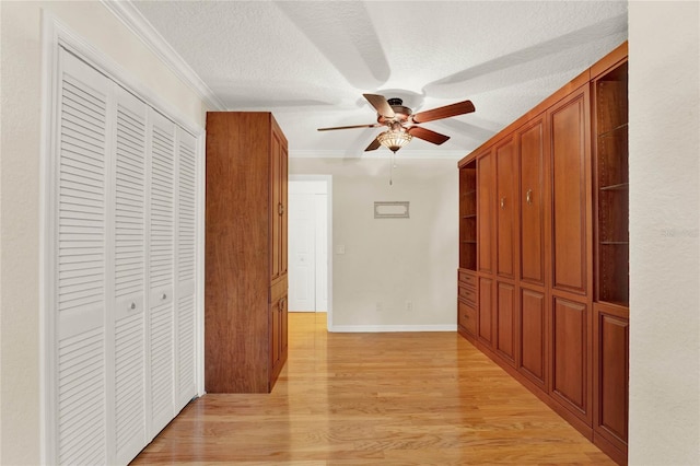 hall featuring light wood-style floors, ornamental molding, a textured ceiling, and baseboards