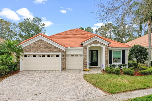 mediterranean / spanish house featuring stone siding, a tiled roof, an attached garage, decorative driveway, and a front yard