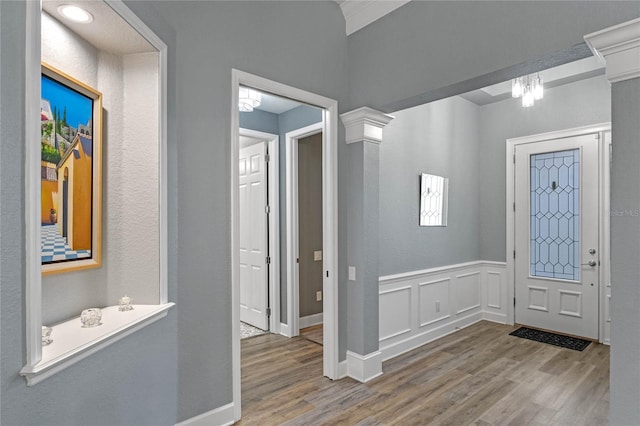 entrance foyer featuring ornate columns, wainscoting, wood finished floors, and a decorative wall