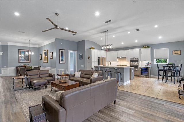 living area featuring wine cooler, visible vents, lofted ceiling, and ceiling fan with notable chandelier