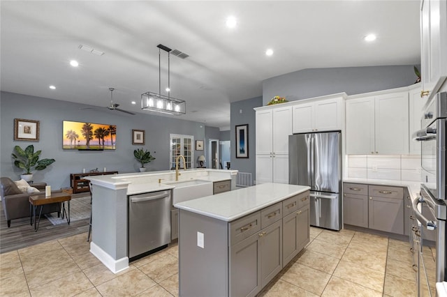 kitchen featuring pendant lighting, stainless steel appliances, gray cabinets, light countertops, and a kitchen island with sink