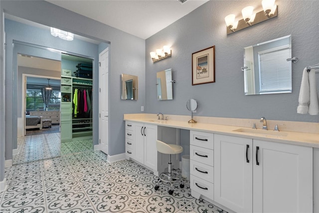 bathroom featuring a walk in closet, a sink, baseboards, and double vanity