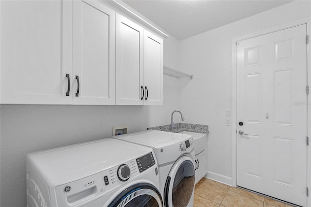 clothes washing area featuring washer and clothes dryer, light tile patterned floors, cabinet space, a sink, and baseboards