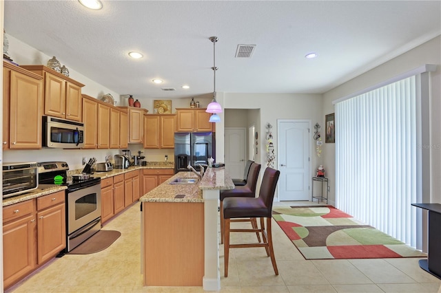 kitchen with decorative light fixtures, a center island with sink, stainless steel appliances, visible vents, and a sink