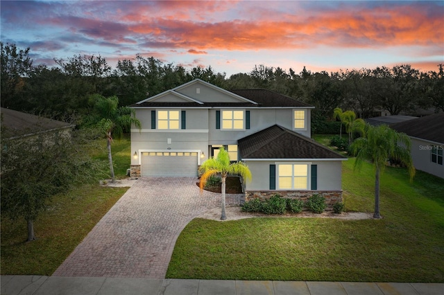 traditional-style home with a garage, stone siding, a yard, decorative driveway, and stucco siding