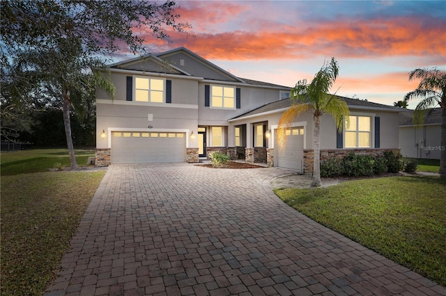 traditional home with decorative driveway, stone siding, a yard, and stucco siding