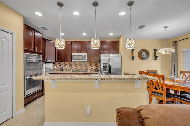 15506 Gemini Dr, Mascotte, FL 34753 - kitchen featuring appliances with stainless steel finishes, decorative light fixtures, a kitchen island with sink, and a breakfast bar area