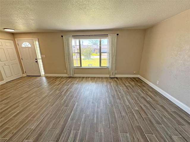 interior space with a textured ceiling, baseboards, wood finish floors, and a textured wall