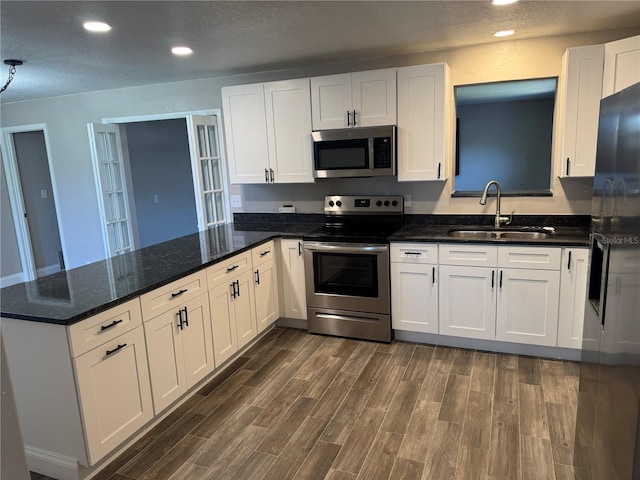 kitchen featuring a sink, dark wood-style floors, white cabinetry, stainless steel appliances, and a peninsula