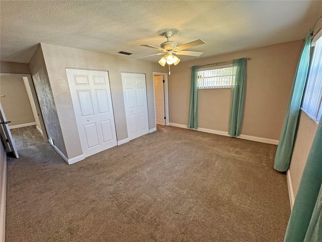 unfurnished bedroom with visible vents, multiple closets, a textured ceiling, and carpet flooring