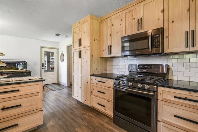 kitchen featuring dark countertops, light brown cabinets, stainless steel appliances, and dark wood-type flooring