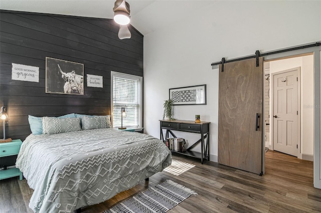 bedroom with high vaulted ceiling, a barn door, wood walls, a ceiling fan, and dark wood-style floors