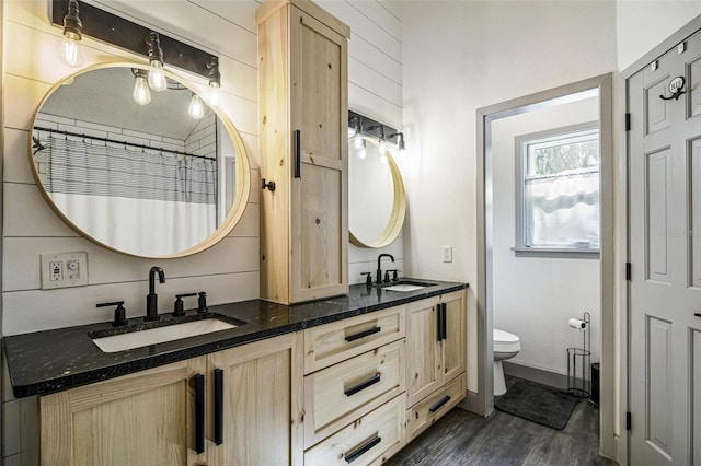 full bathroom featuring toilet, double vanity, a sink, and wood finished floors