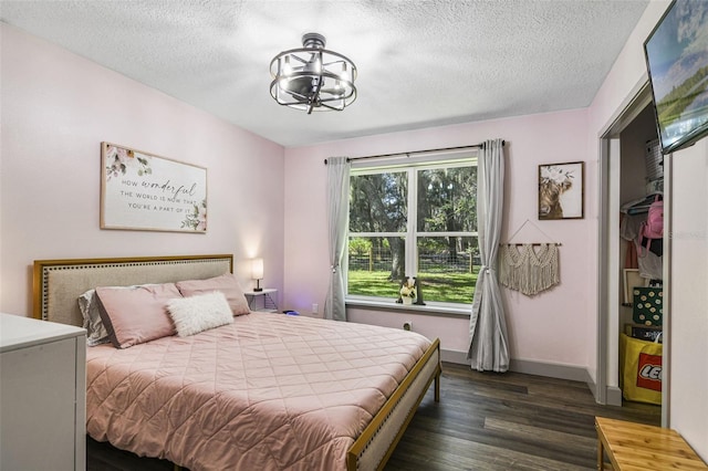 bedroom featuring a chandelier, dark wood finished floors, a textured ceiling, and baseboards