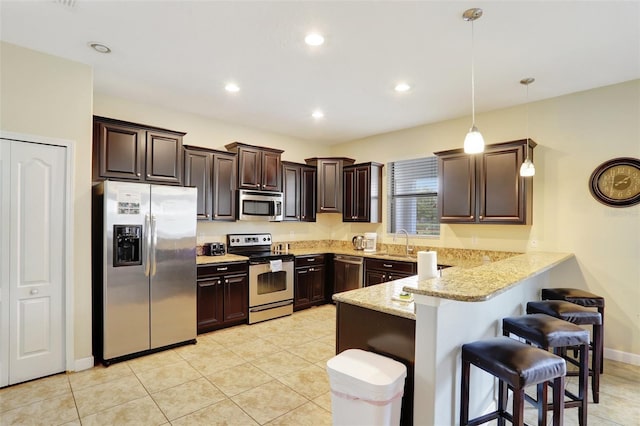 kitchen featuring a breakfast bar area, stainless steel appliances, dark brown cabinetry, decorative light fixtures, and kitchen peninsula