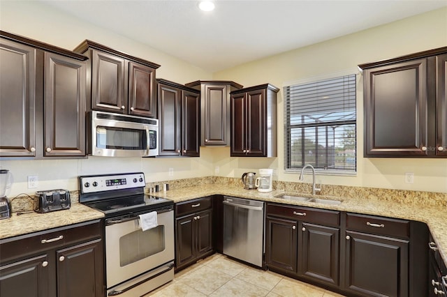 kitchen featuring sink, dark brown cabinets, light tile patterned floors, stainless steel appliances, and light stone countertops