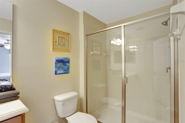 bathroom with a shower with door, vanity, ceiling fan, and toilet