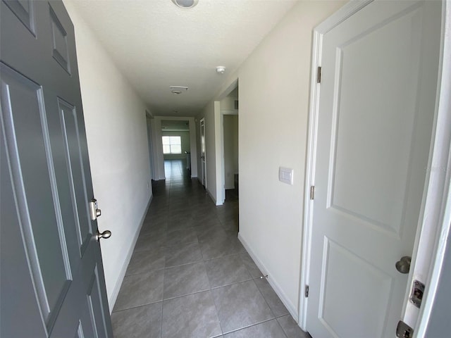 corridor featuring tile patterned flooring, baseboards, and a textured ceiling