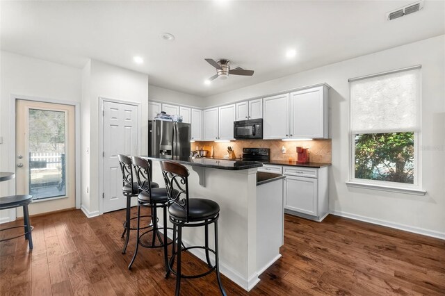 231 Turtle Cv, Panama City Beach, FL 32413 - kitchen with white cabinetry, dark hardwood / wood-style flooring, a kitchen breakfast bar, a center island, and black appliances