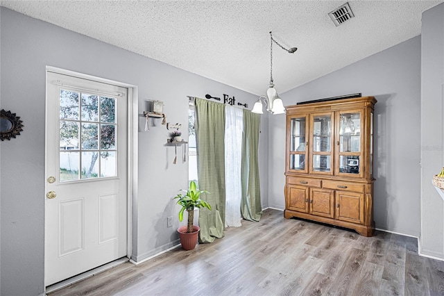 dining area featuring vaulted ceiling, a textured ceiling, a notable chandelier, and light hardwood / wood-style floors