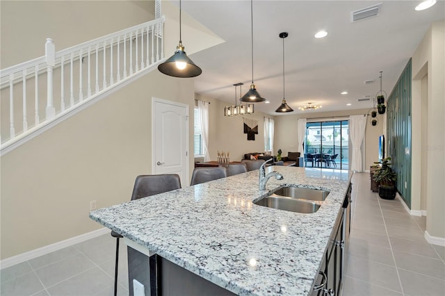 kitchen featuring light tile patterned flooring, pendant lighting, sink, a kitchen island with sink, and light stone countertops