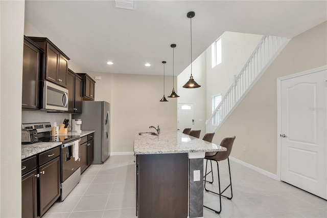 kitchen with a kitchen bar, sink, hanging light fixtures, an island with sink, and stainless steel appliances