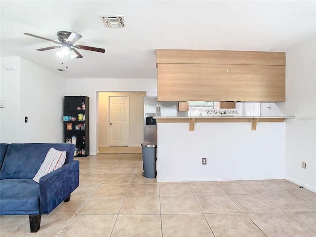 kitchen featuring ceiling fan, a kitchen bar, kitchen peninsula, and light tile patterned floors