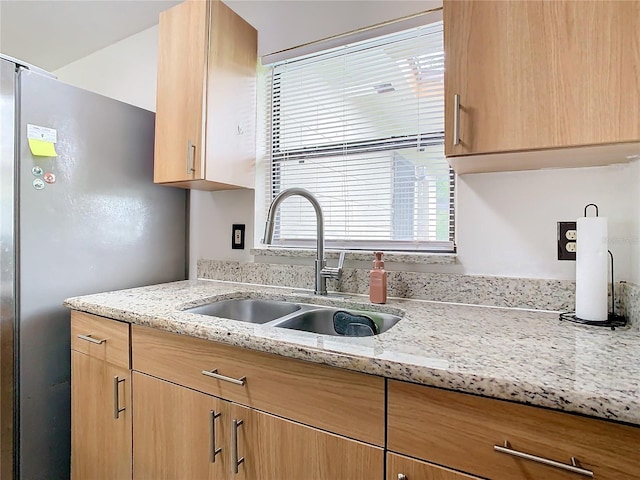 kitchen featuring light stone counters, sink, stainless steel refrigerator, and light brown cabinetry