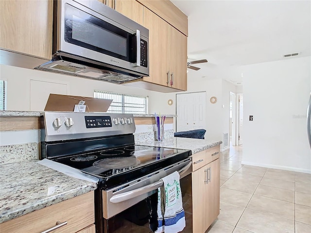 kitchen featuring light tile patterned flooring, light stone counters, light brown cabinets, appliances with stainless steel finishes, and ceiling fan