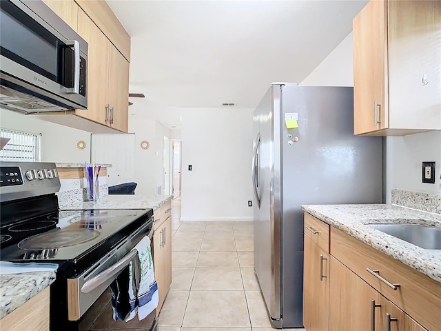 kitchen with stainless steel appliances, light stone countertops, light brown cabinets, and light tile patterned floors