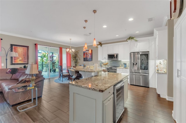 kitchen featuring decorative light fixtures, an island with sink, white cabinets, beverage cooler, and stainless steel appliances