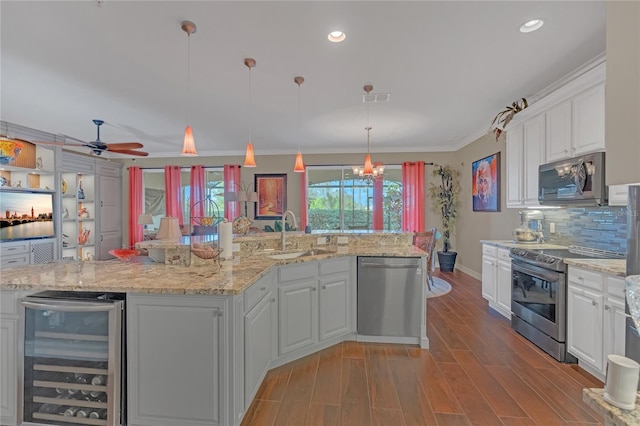 kitchen with sink, appliances with stainless steel finishes, hanging light fixtures, wine cooler, and white cabinets