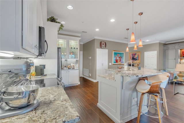 kitchen featuring decorative light fixtures, appliances with stainless steel finishes, white cabinets, and a center island with sink