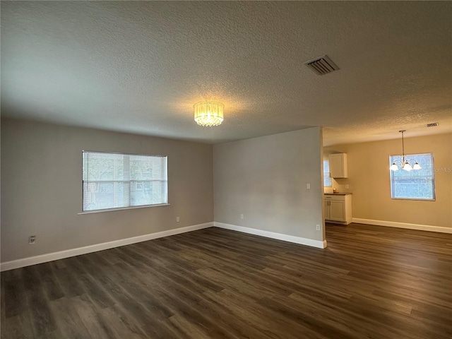 empty room featuring dark hardwood / wood-style flooring, a healthy amount of sunlight, a textured ceiling, and an inviting chandelier