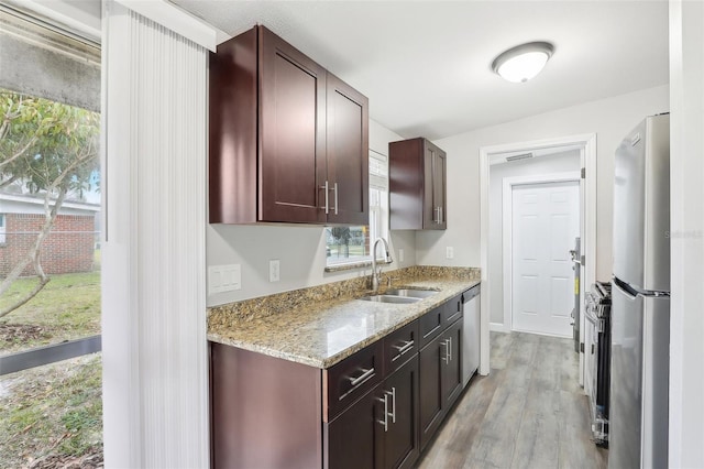 kitchen with light wood-type flooring, stainless steel appliances, light stone countertops, and sink