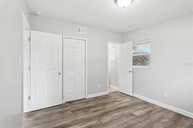 unfurnished bedroom featuring a textured ceiling, a closet, and wood-type flooring