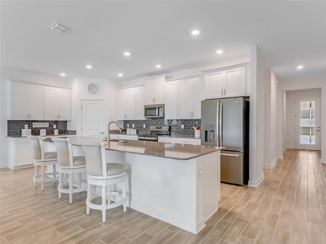 kitchen with white cabinetry, appliances with stainless steel finishes, sink, and a center island with sink