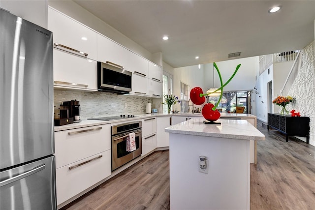 kitchen featuring appliances with stainless steel finishes, backsplash, white cabinets, a center island, and light hardwood / wood-style floors