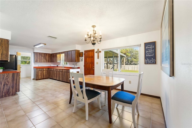 tiled dining space with sink, a notable chandelier, and a textured ceiling