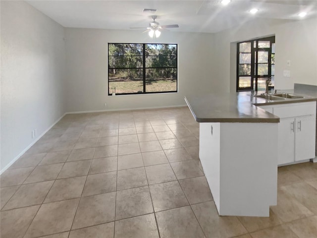 kitchen with kitchen peninsula, sink, ceiling fan, white cabinets, and light tile patterned flooring