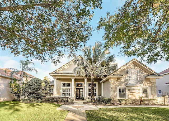 view of front of house with stone siding, a balcony, a front lawn, and stucco siding