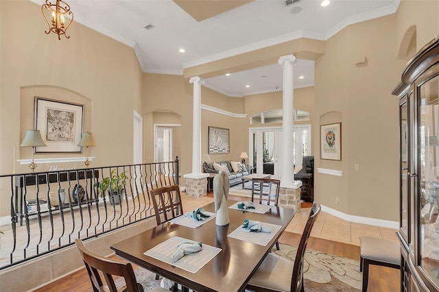 dining room featuring decorative columns, baseboards, a high ceiling, crown molding, and light wood-style floors