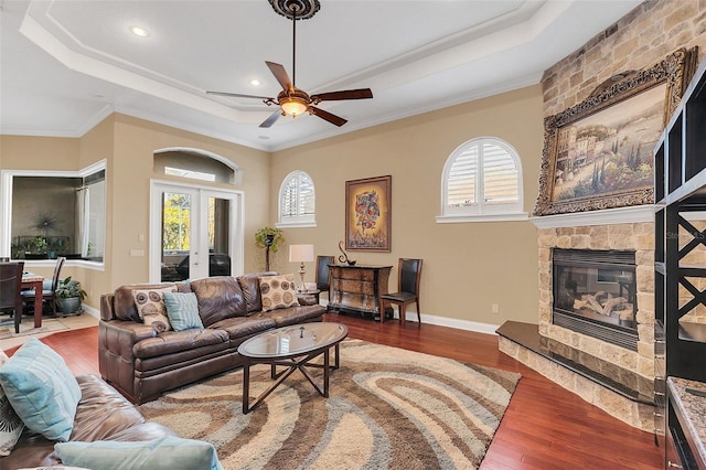 living room featuring french doors, wood finished floors, a raised ceiling, and a stone fireplace